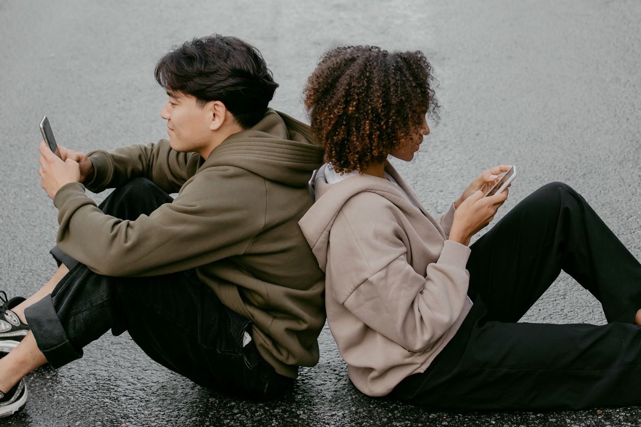 A couple sitting back to back, both absorbed in their phones