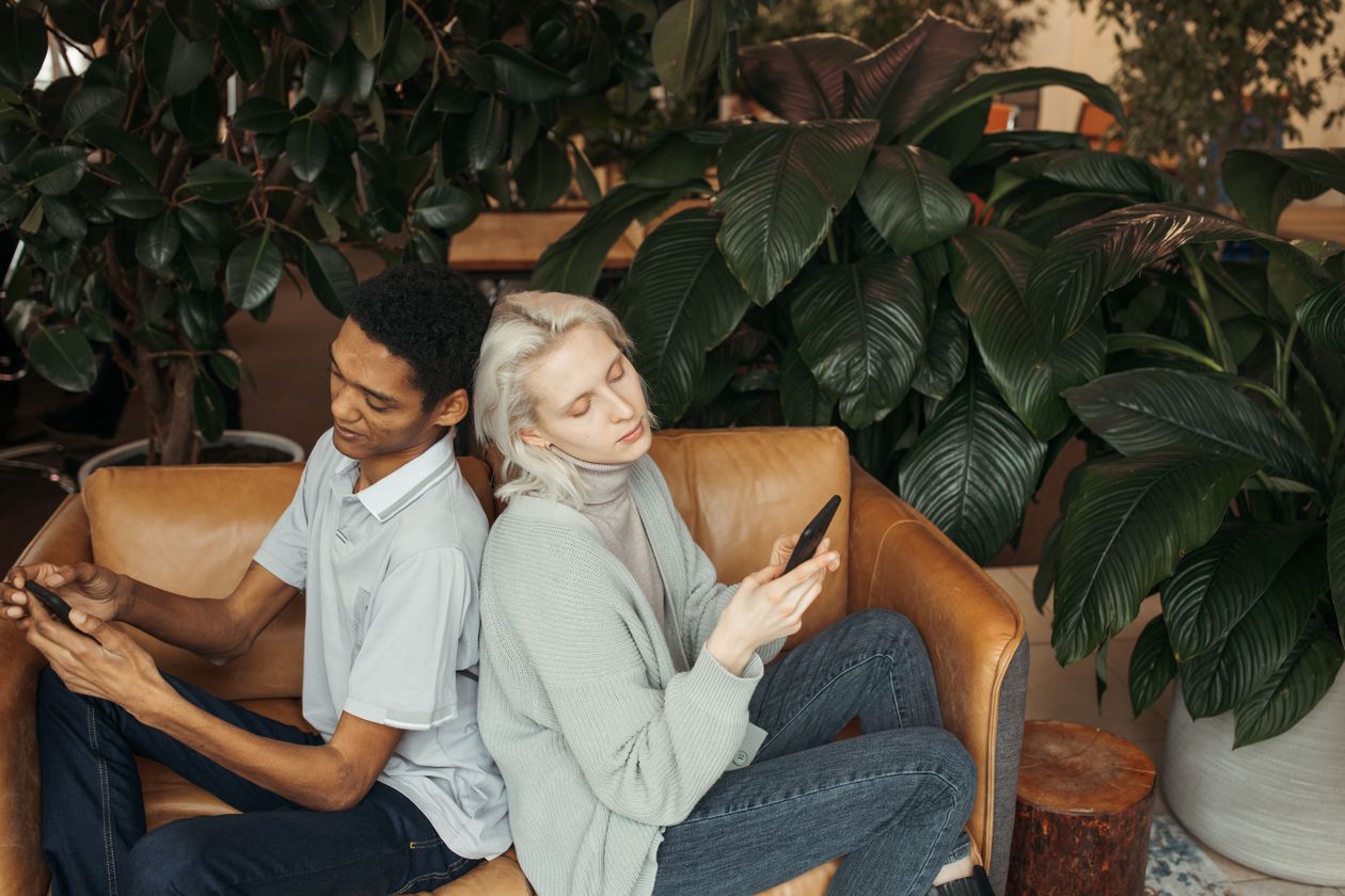 A couple sitting apart, each distracted by their own phone