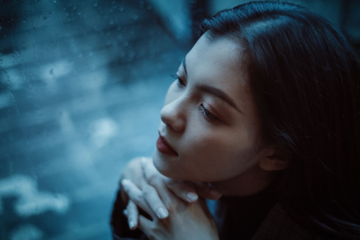 A woman standing alone at a window, lost in thought